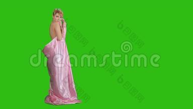 穿着粉红色缎子床单的可爱的金发女郎在色度键背景下为相机做姿势
